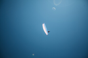 A skydiver flies between mountains. A paraglider flies against a clear sky. Paragliding in the mountains. Glare from the sun © Svetlana