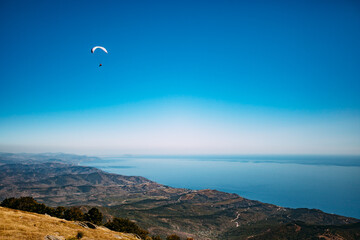 A skydiver flies between mountains. A paraglider flies against a background of clear sky and...