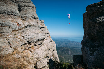 A skydiver flies between mountains. A paraglider flies against a clear sky and a mountain...