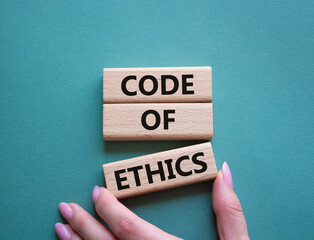 Code of ethics symbol. Concept words Code of ethics on wooden blocks. Beautiful grey green background. Businessman hand. Business and Code of ethics concept. Copy space.