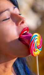 Young sexy brunette latina with bright red sensual lips passionately licking a colorful spiral...
