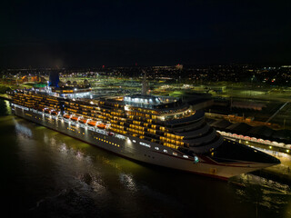 Cruise ship with Union Jack Flag at night with dark sky at Southampton Port, UK. Lower altitude aerial view on the side of the cruise ship with lights before departure. Illuminated car terminal.