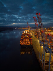 Beautiful container ship stern lights with reflection at dusk. Tall port cranes in Southampton...