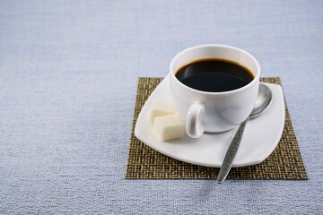 White cup of black coffee with sugar on a napkin-mat and a beautiful saucer on the table early in the morning