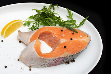 Raw salmon steak on a white plate with lemon and herbs