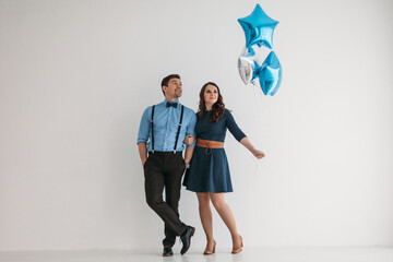 A couple in love with balloons on a white wall background. The man is wearing a blue shirt,...