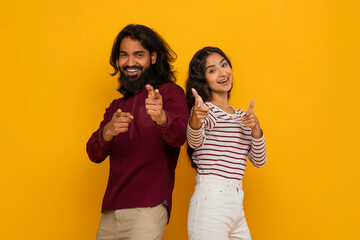 Positive young indian man and woman pointing at camera