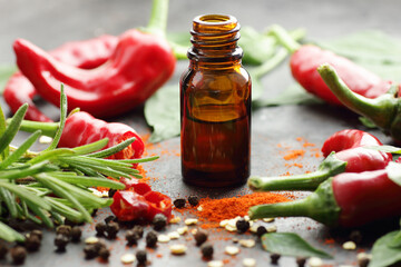 Red chili pepper oil, tincture, extract or vinegar with fresh vegetables and leaves on black table,...