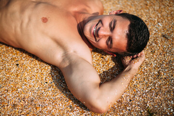 A man is lying on the sand on the beach. One hand is raised to the head. View from above. A wave is...