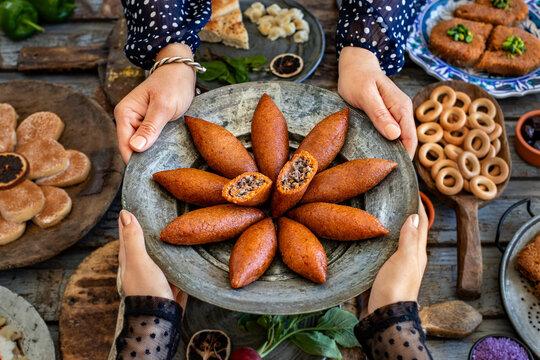 Hands of two women holding kibbeh plate . Turkish name is oruk or i&ccedil;li k&ouml;fte or icli kofte . Dinner table with many meals on the table.  
