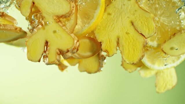 Super Slow Motion of Falling Ginger and Lemon Pieces into Water. Isolated on Colored Background. Filmed on High Speed Cinema Camera, 1000 fps.