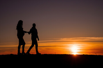 a man and a pregnant woman holding hands against a background of sunset, sea, ocean