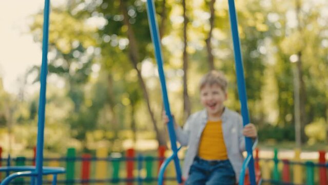 Cheerful little boy swinging and laughing on playground in park, happy childhood