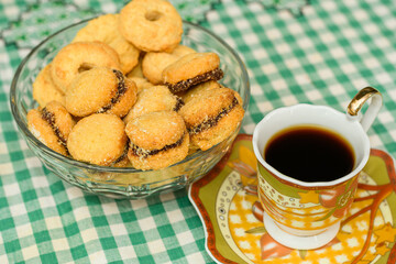 Coffee in a traditional porcelain cup and biscuits filled with guava paste over a tablecloth with rustic checkered texture. Breakfast or afternoon snack concept.