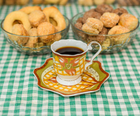 Coffee in a traditional porcelain cup over a tablecloth with rustic checkered texture and some biscuits blurred on the background. Breakfast or afternoon snack concept.