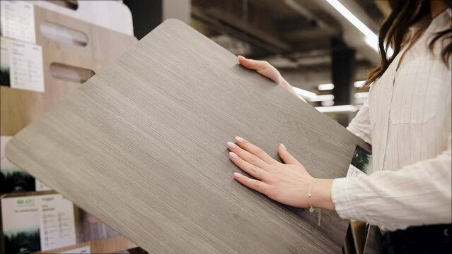 Close-up of a young woman's hand examines a laminate floor in a hardware store. Woman holding parquet board panel sample