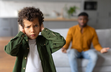 Black child boy covering ears with parent arguing on background