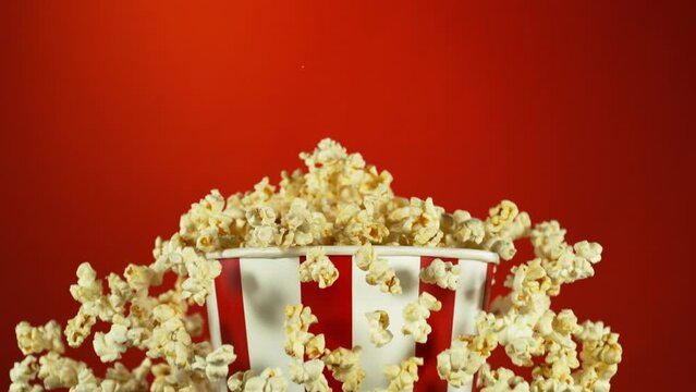 Super Slow Motion of Exploding popcorn from Bucket. Isolated on Red Background. Studio Shot of Flying Food. Filmed on High Speed Cinema Camera, 1000fps. Speed Ramp Effect.