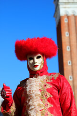 masked person with red headdress during the Venice carnival with Saint Mark bell tower in the background