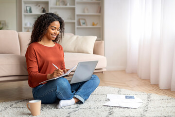 Young Smiling Black Woman Using Laptop At Home And Taking Notes