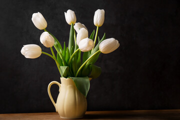 A bouquet of white tulips in a yellow jug