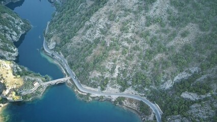 The aerial view shows a winding road snaking through the rugged mountains, surrounded by lush...