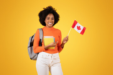 Smiling young woman with afro hair, dressed in an orange sweater and white jeans