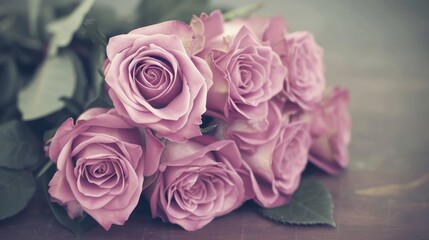 a bunch of pink roses sitting on top of a wooden table next to a bunch of green leaves on top of a table.