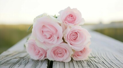 a bouquet of pink roses sitting on top of a wooden table in front of a blurry background of grass.