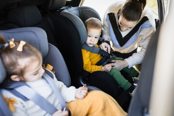 Side view of two children in baby car seats and mother fastening seat belts.