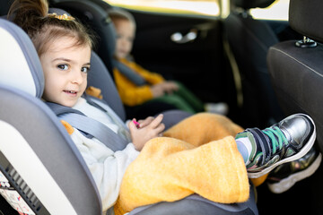 Cheerful passenger girl in car booster seat. Family road trip concept.