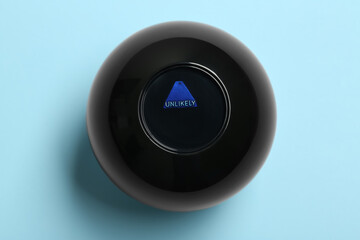 Magic eight ball with prediction Unlikely on light blue background, top view - obrazy, fototapety, plakaty