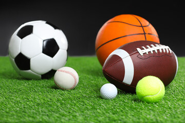 Many different sports balls on green grass against black background