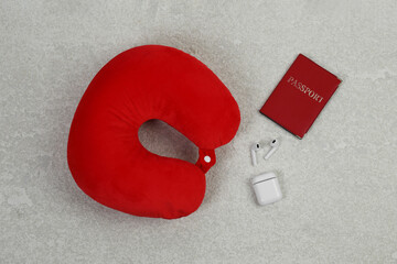 Soft travel pillow, passport and earphones on grey textured background, flat lay