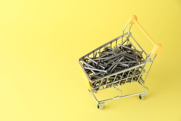 Metal nails in shopping cart on yellow background, space for text