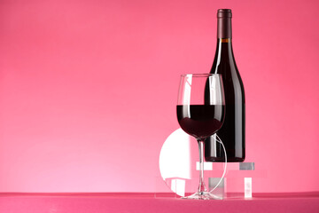 Stylish presentation of delicious red wine in bottle and glass on pink background. Space for text