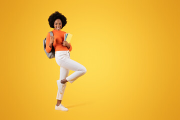Energetic young woman with a joyous smile jumps in the air, notebooks in hand