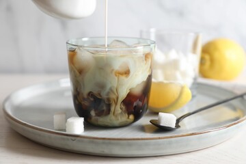 Pouring milk into glass with refreshing iced coffee at white wooden table, closeup