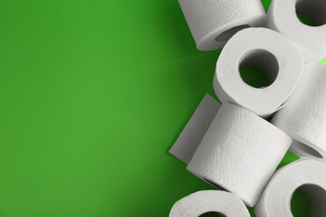 Soft toilet paper rolls on green background, flat lay. Space for text