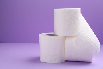 Soft toilet paper rolls on violet background, closeup. Space for text