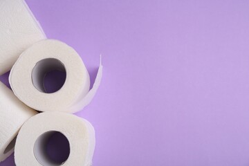 Soft toilet paper rolls on violet background, flat lay. Space for text