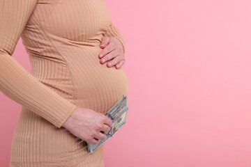 Surrogate mother. Pregnant woman with dollar banknotes on pink background, closeup. Space for text