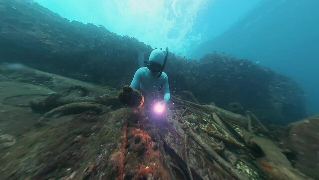 Freediver swims underwater in the sea and explores remains of the shipwreck
