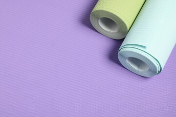 Two colorful wallpaper rolls on violet sample, above view. Space for text