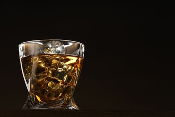 Whiskey with ice cubes in glass on table against black background. Space for text