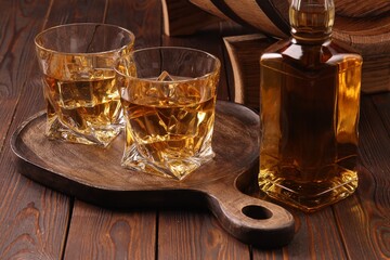 Whiskey with ice cubes in glasses and bottle on wooden table