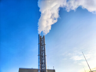 Air pollution by smoke coming out of factory chimney. White clouds of smoke against a blue sky background