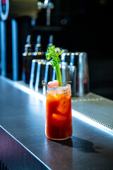 Camarera de cocktail bar prepara bloody Mary sobre una barra de un cocktail bar exclusivo en ambiente nocturno con detalle sobre el cocktail exquisito