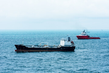 Oil tanker ship sailing through calm, blue waters inside sea port in Singapore.