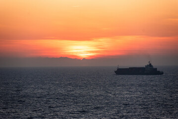 Sunset sky over the calm ocean -  
silhouette of the cargo ship on her lonely journey. 
